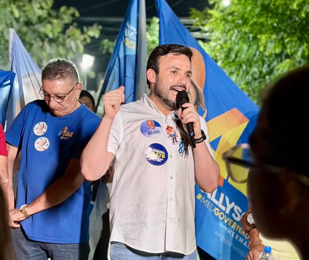 Dr. Tadeu fala ao microfone, diante de bandeiras e apoiadores, durante uma caminhada da campanha eleitoral em Caicó.