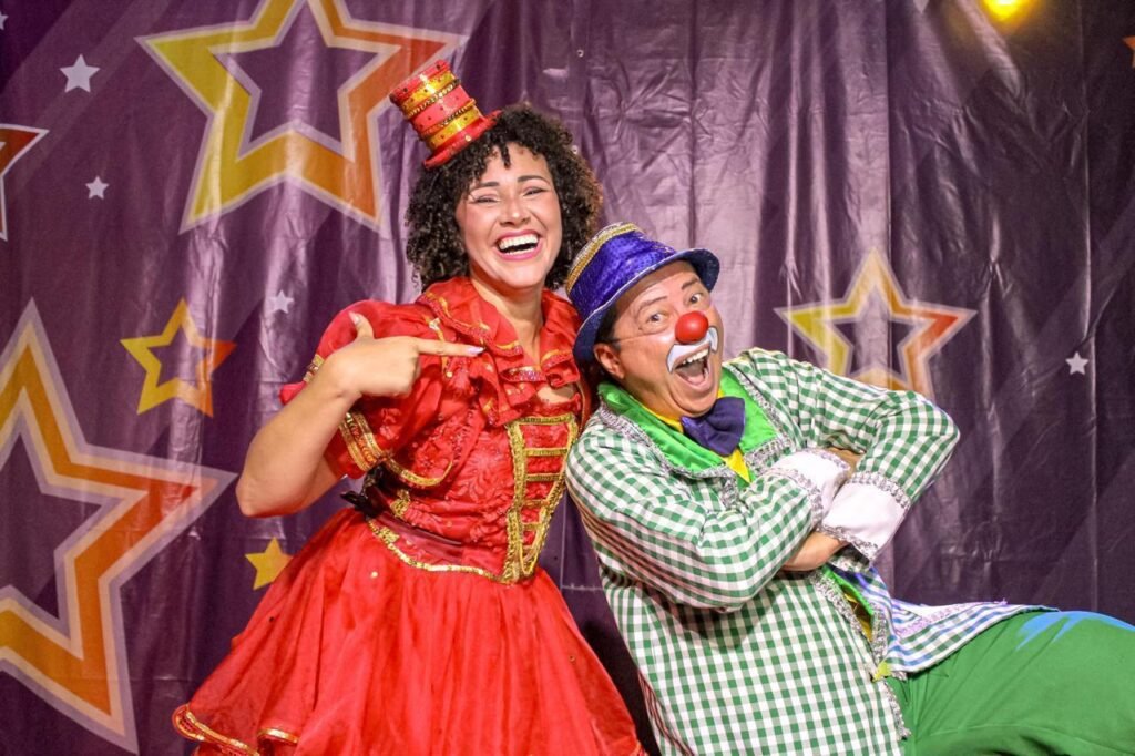 Dois artistas caracterizados como palhaços posam diante de uma cortina com estrelas.
