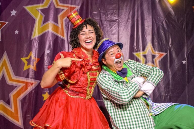 Dois artistas caracterizados como palhaços posam diante de uma cortina com estrelas.