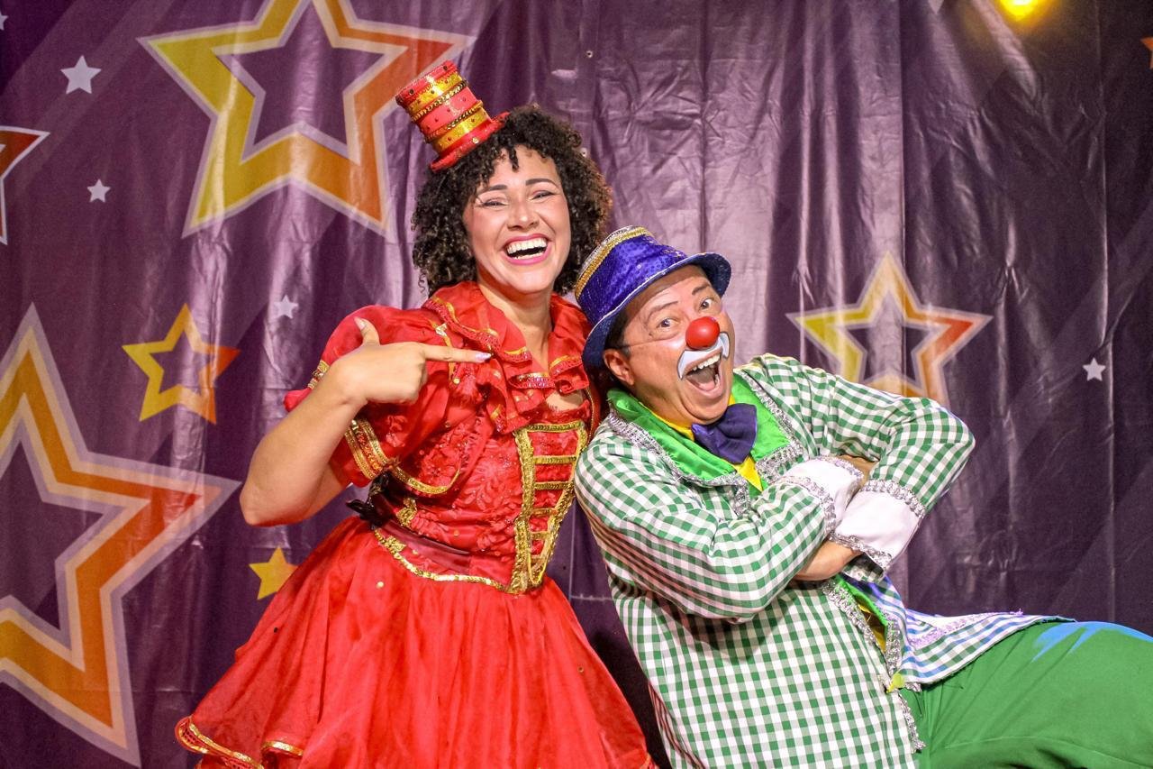 Dois artistas caracterizados como palhaços posam diante de uma cortina com estrelas.
