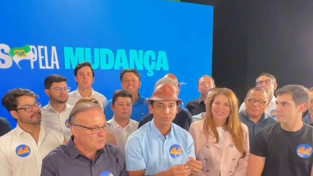 Pessoas reunidas diante de um painel azul no registro do anúncio de apoio.