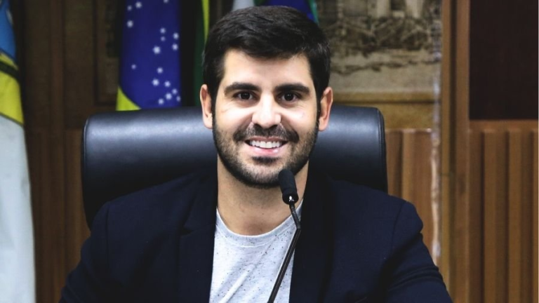 Robson Carvalho sentado à mesa com microfone.